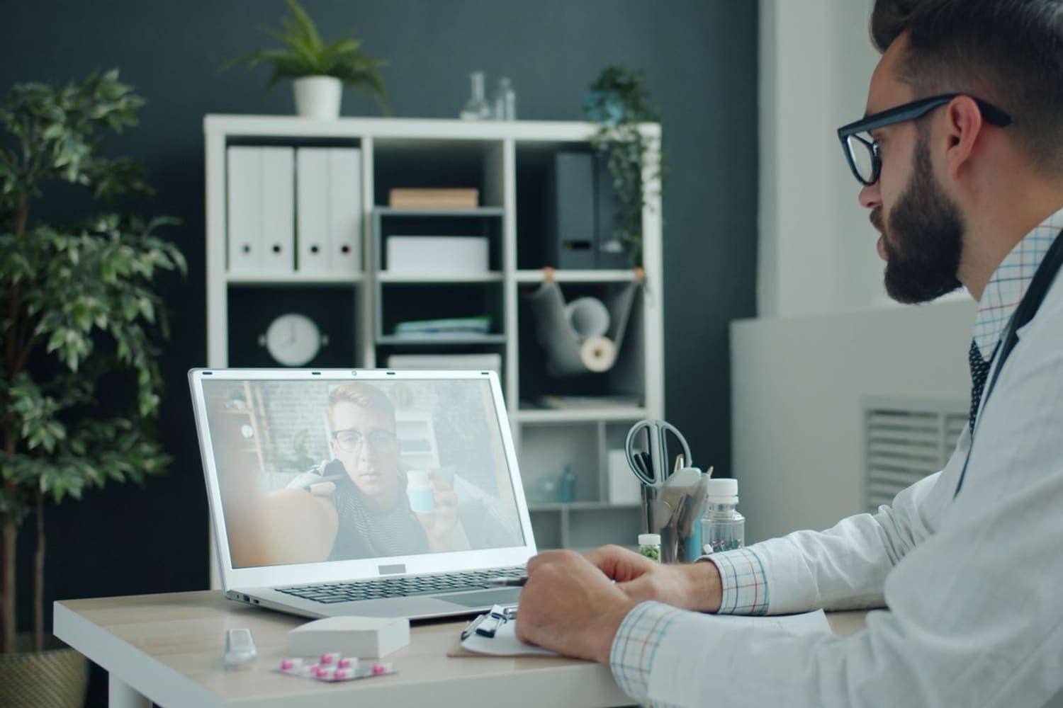 GP in a white coat holding a video consultation with a patient from an online clinic